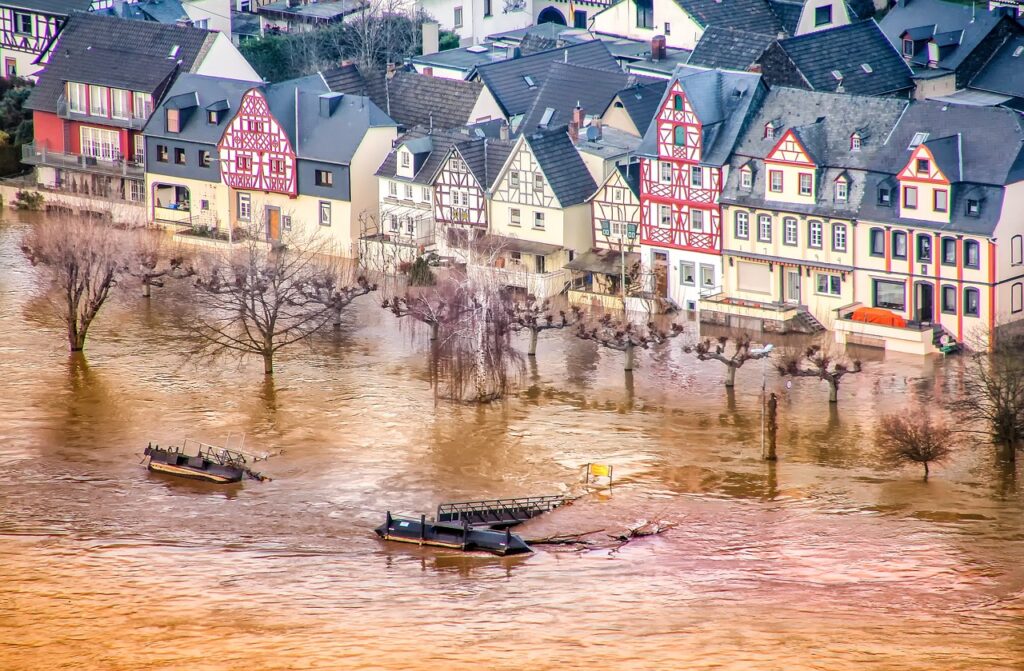 Vue aérienne d'une ville historique inondée avec des maisons à colombages bordant un fleuve en crue, illustrant les dégâts structurels nécessitant une intervention de démolition après sinistre.